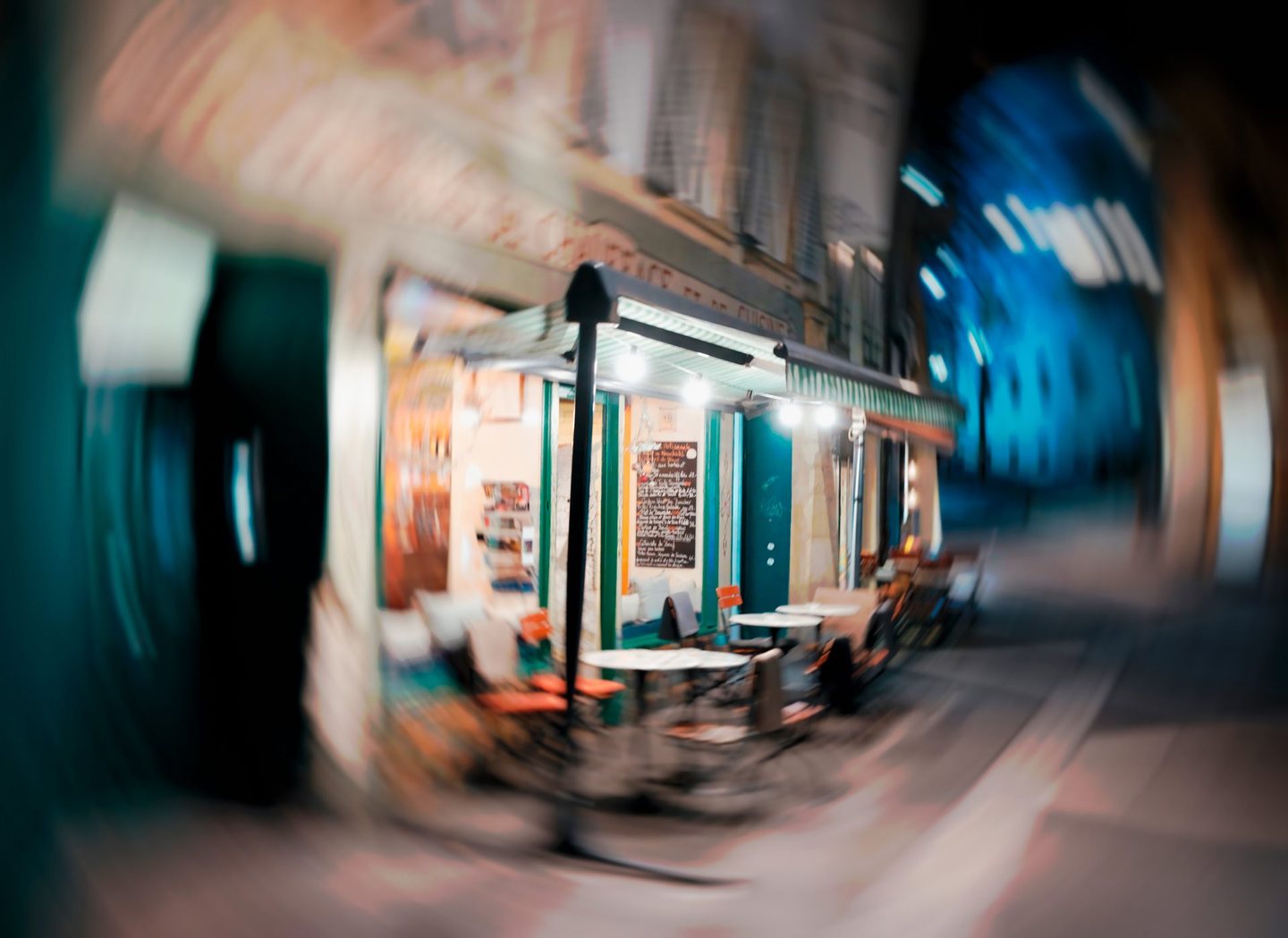 La terrasse d'un café éclairée le soir, rue des Moulins ; la scène tourne en un flou circulaire de bleus et d'oranges.